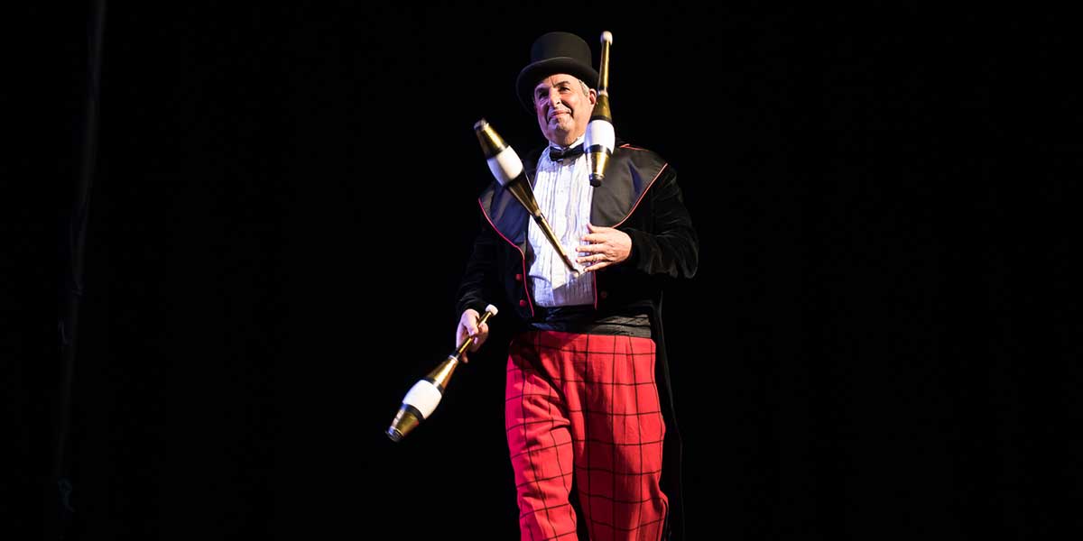 photo of a juggler performing with three clubs on stage